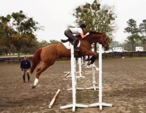 Glazer clears a jump in Ocala, FL. Watching in the background is Neal Shapiro, an Olympic medalist in the 1972 Munich Games, who is working with the young equestrienne. 